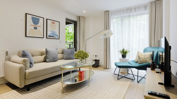 Una sala de estar moderna con un sofá, una mesa de centro de vidrio, un sillón azul, un televisor y obras de arte en la pared.