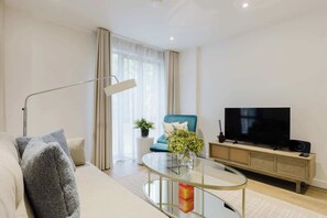 A modern living room with a sofa, a glass coffee table, a blue armchair, a TV, and a side table with a plant. - Stylish 1BDR Flat with Private Balcony in Vauxhall (London)