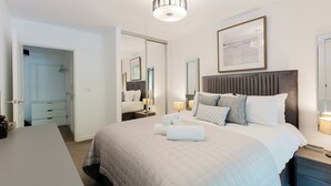 Habitación de hotel con cama, mesitas de noche, escritorio, armario y espejo.