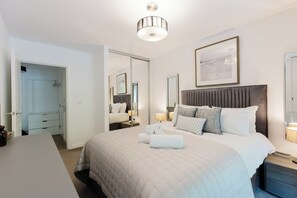 A hotel room with a bed, bedside tables, a desk, a wardrobe, and a mirror. - Stylish 1BDR Flat with Private Balcony in Vauxhall (London)