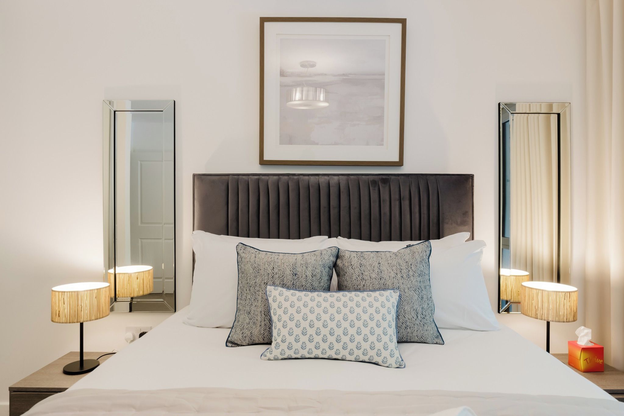 A neatly made bed with a headboard, two bedside lamps, and a framed picture above the bed.