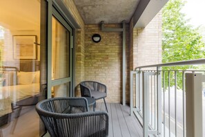 A balcony with a glass door leading to a room, a round wall clock, and two wicker chairs. - Stylish 1BDR Flat with Private Balcony in Vauxhall (London)