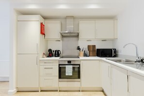 A compact kitchen with white cabinetry, a built-in oven, a microwave, and a stainless steel sink. - Stylish 1BDR Flat with Private Balcony in Vauxhall (London)