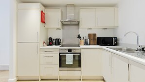 Cocina compacta con muebles blancos, extractor de acero inoxidable, microondas y horno empotrado.