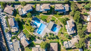 Oversigtsbillede af et boligområde med flere huse, en central swimmingpool og grønt areal omkring.