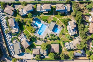 Ett flygbildsbild av ett bostadsområde med flera hus, en central pool och omgivande grönska.