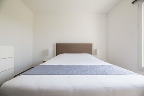 Uma cama com cabeceira, luminárias de mesa e uma janela.