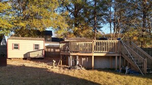 Une terrasse en bois avec un escalier, un petit abri de jardin et une maison en arrière-plan.