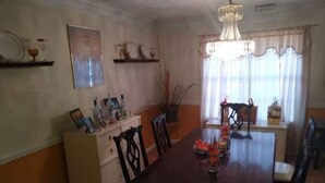 Une salle à manger avec une table en bois, des chaises, un lustre et une fenêtre avec des rideaux.