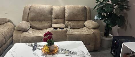 A living room with a beige sofa, a marble coffee table, a potted plant, and a speaker.