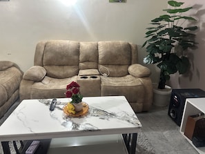 A living room with a beige sofa, a marble coffee table, a potted plant, and a speaker.