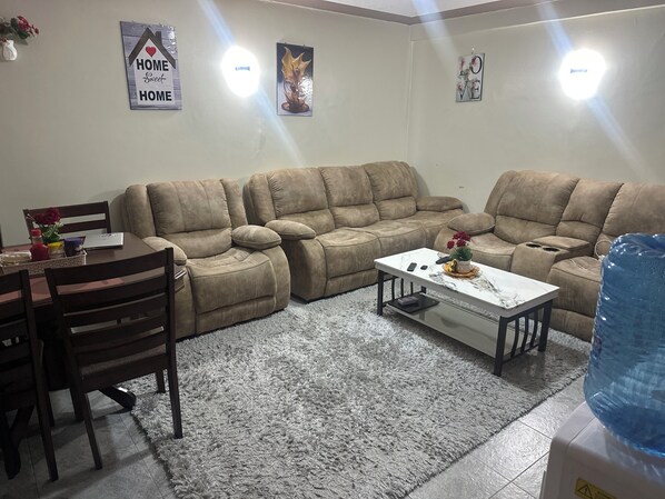 A living room with a beige sectional sofa, a small white table, and a grey shaggy rug.