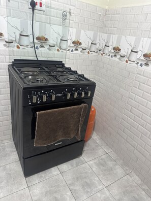 A black stove with a brown towel hanging on the oven door, a gas connection, and a tiled backsplash with kitchenware illustrations.