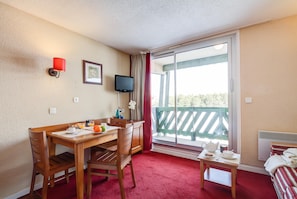 A hotel room with a wooden desk, chairs, a television, a balcony with a view, and a bed with striped bedding. - Charming Pyrenees Mountain Getaway (Bolquere)