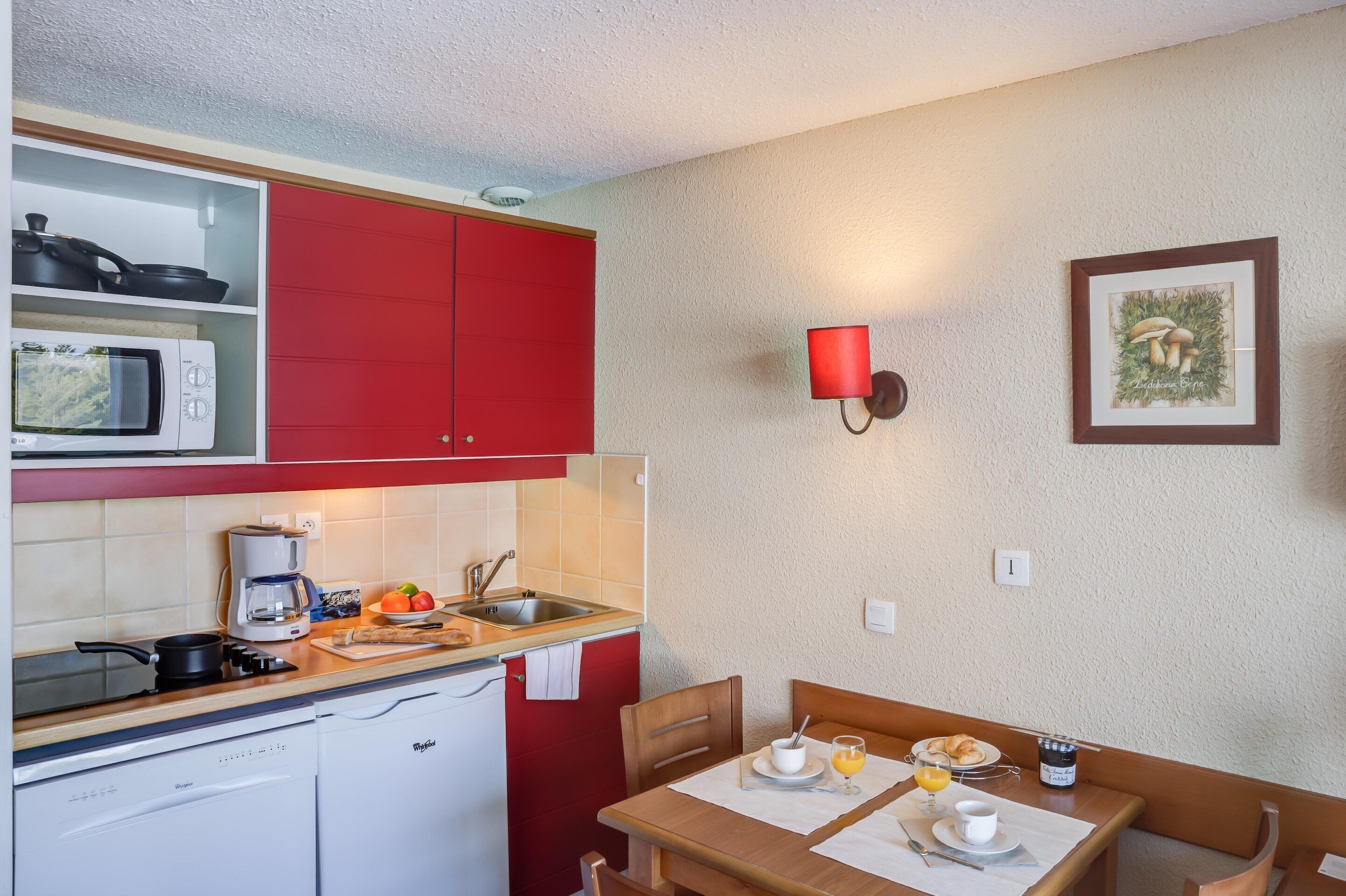 A compact kitchen with red cabinets, a microwave, a coffee maker, and a dining area with a table set for breakfast.