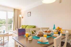 A dining area with a table set for breakfast, including bread, pastries, and orange juice. - Branville Duplex Apartment for 6 (Branville)