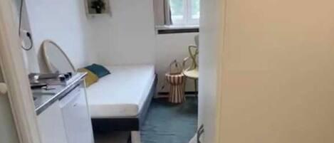 A small, compact room with a kitchenette, a bed, and a small table.