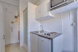 Eine kleine Küche mit integriertem Mikrowellenherd, Spüle und kompaktem Kühlschrank.