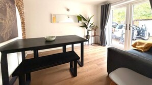 A modern living room with a dark wooden dining table, a sofa, and a large window with a view of parked cars. - Swan View House in Littleport (Littleport)