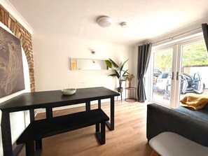 Ein modernes Wohnzimmer mit einem schwarzen Esstisch, einer Couch und einem großen Fenster mit Blick auf geparkte Autos.