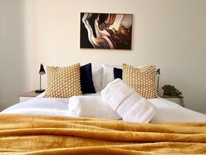 A neatly made bed with white and gold pillows, a mustard-colored blanket, and a painting on the wall. - Swan View House in Littleport (Littleport)