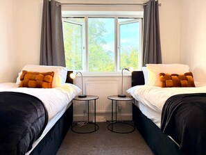 A room with two beds, a window with curtains, a radiator, and a lamp on a small table. - Swan View House in Littleport (Littleport)