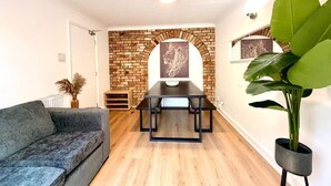 A modern living room with a brick fireplace, a dining table, a sofa, and a large green plant. - Swan View House in Littleport (Littleport)