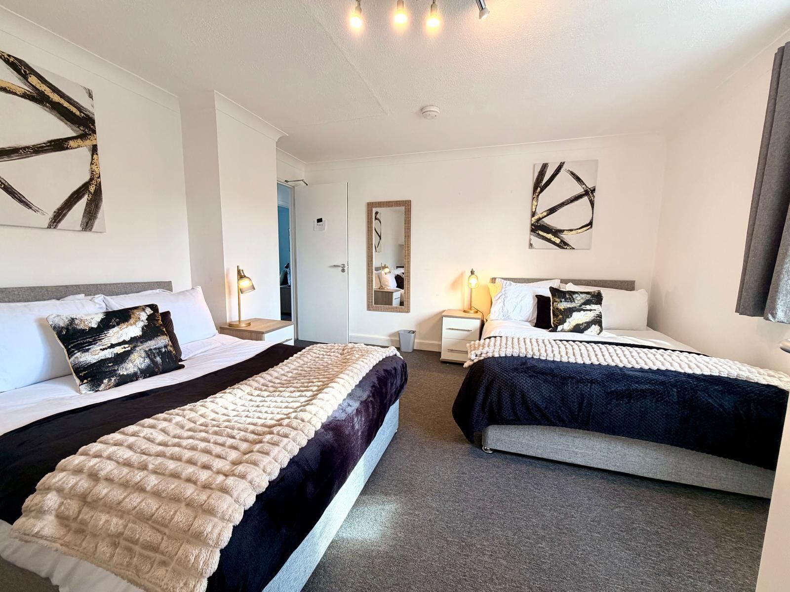 Ein Hotelzimmer mit zwei Betten, einem Nachttisch mit Lampe, einem Spiegel und abstrakter Wandkunst.