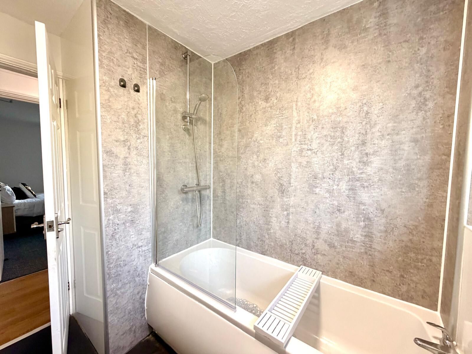 A modern bathroom with a glass-enclosed shower, a freestanding bathtub, and a textured wall.