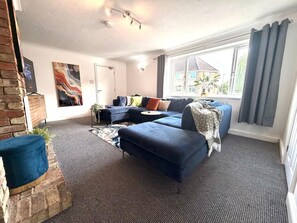 A modern living room with a sectional sofa, a fireplace, and a large window with curtains. - Swan View House in Littleport (Littleport)