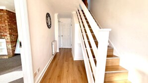 A hallway with a wooden floor, white walls, a white door, and a white staircase with a banister. - Swan View House in Littleport (Littleport)