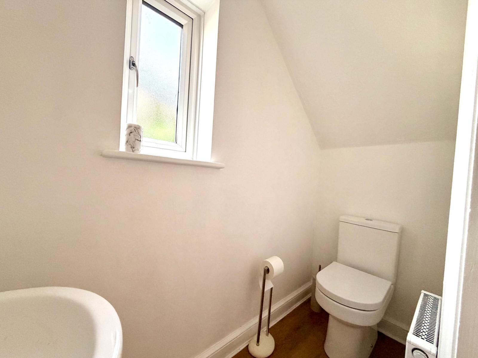 A small, white bathroom with a window, a toilet, a radiator, and a white bathtub.