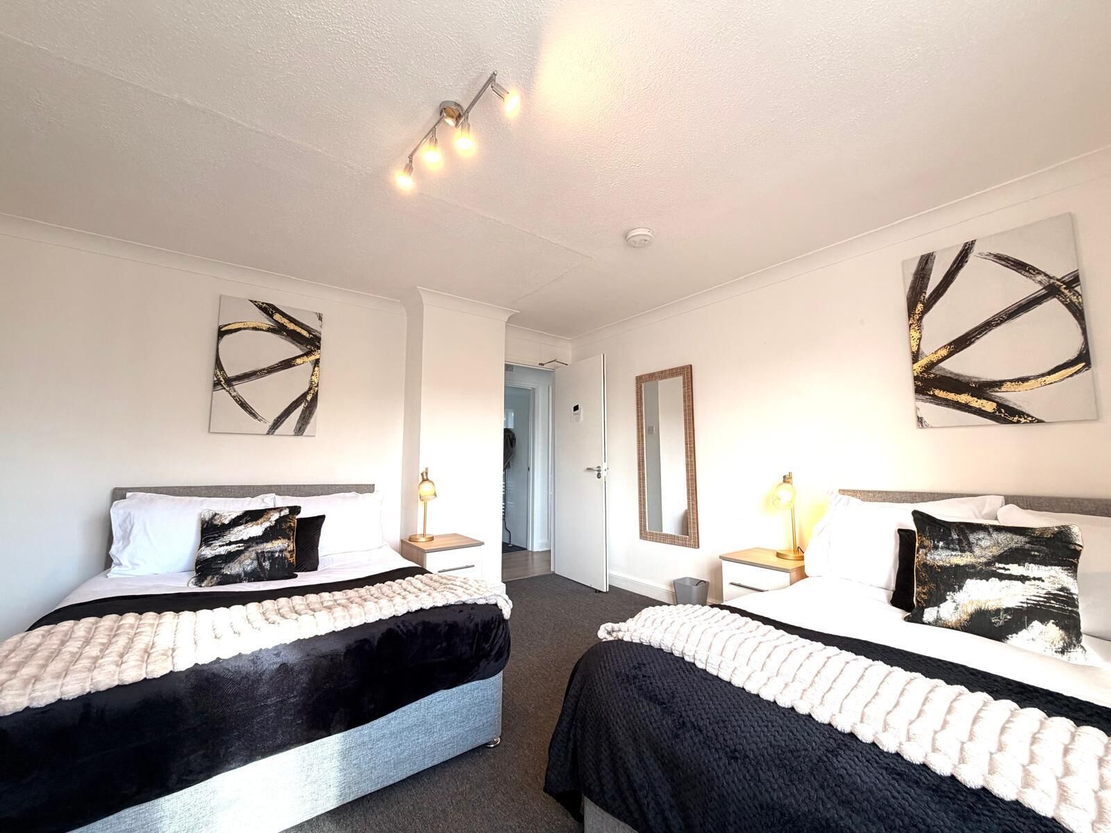 A hotel room with two beds, a mirror, abstract wall art, and a ceiling light fixture.