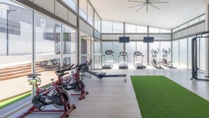 Ein modernes Fitnessstudio mit Cardiogeräten, Rudergerät und einem Bereich mit grünem Kunstrasen.