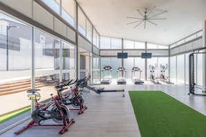 Ein modernes Fitnessstudio mit Cardiogeräten, Rudergerät und einem Bereich mit grünem Kunstrasen.