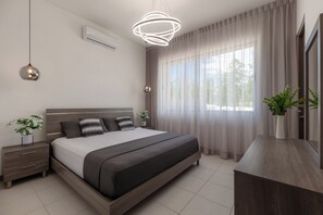 Ein modernes Schlafzimmer mit Bett, Nachttischen, einem Schreibtisch und einem großen Fenster mit Vorhängen.