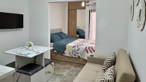Ett kompakt sovrum med en säng, en soffa, ett skrivbord och en tv.