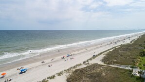 A beach with a long stretch of sand, a few umbrellas, and a few people. - Sunrise Retreat Private Pool & Hot Tub. Golfers Delight. Steps to the beach. (North Myrtle Beach)
