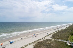 Ein Strand mit einer weiten Sandfläche, einigen Sonnenschirmen und wenigen Personen.