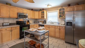 A kitchen with wooden cabinets, a stainless steel refrigerator, a microwave, a stove, and a ceiling fan. - Sunrise Retreat Private Pool & Hot Tub. Golfers Delight. Steps to the beach. (North Myrtle Beach)