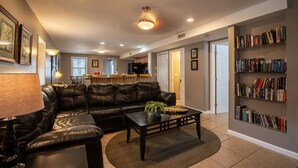 A living room with a leather sofa, a coffee table, a bookshelf, and a dining area in the background. - Sunrise Retreat Private Pool & Hot Tub. Golfers Delight. Steps to the beach. (North Myrtle Beach)