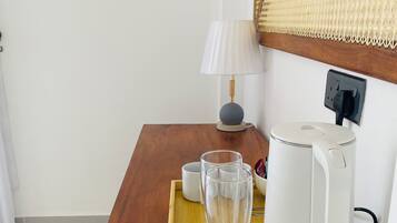 Une table de chevet en bois sur laquelle se trouvent une bouilloire blanche, un verre transparent et une tasse blanche, le tout posé sur un plateau.