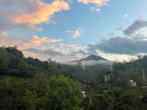 A hilly landscape with scattered buildings, dense greenery, and a partly cloudy sky.