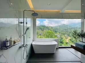 Une salle de bain moderne avec une baignoire sur pieds, une douche en verre et une grande fenêtre donnant sur un paysage montagneux.