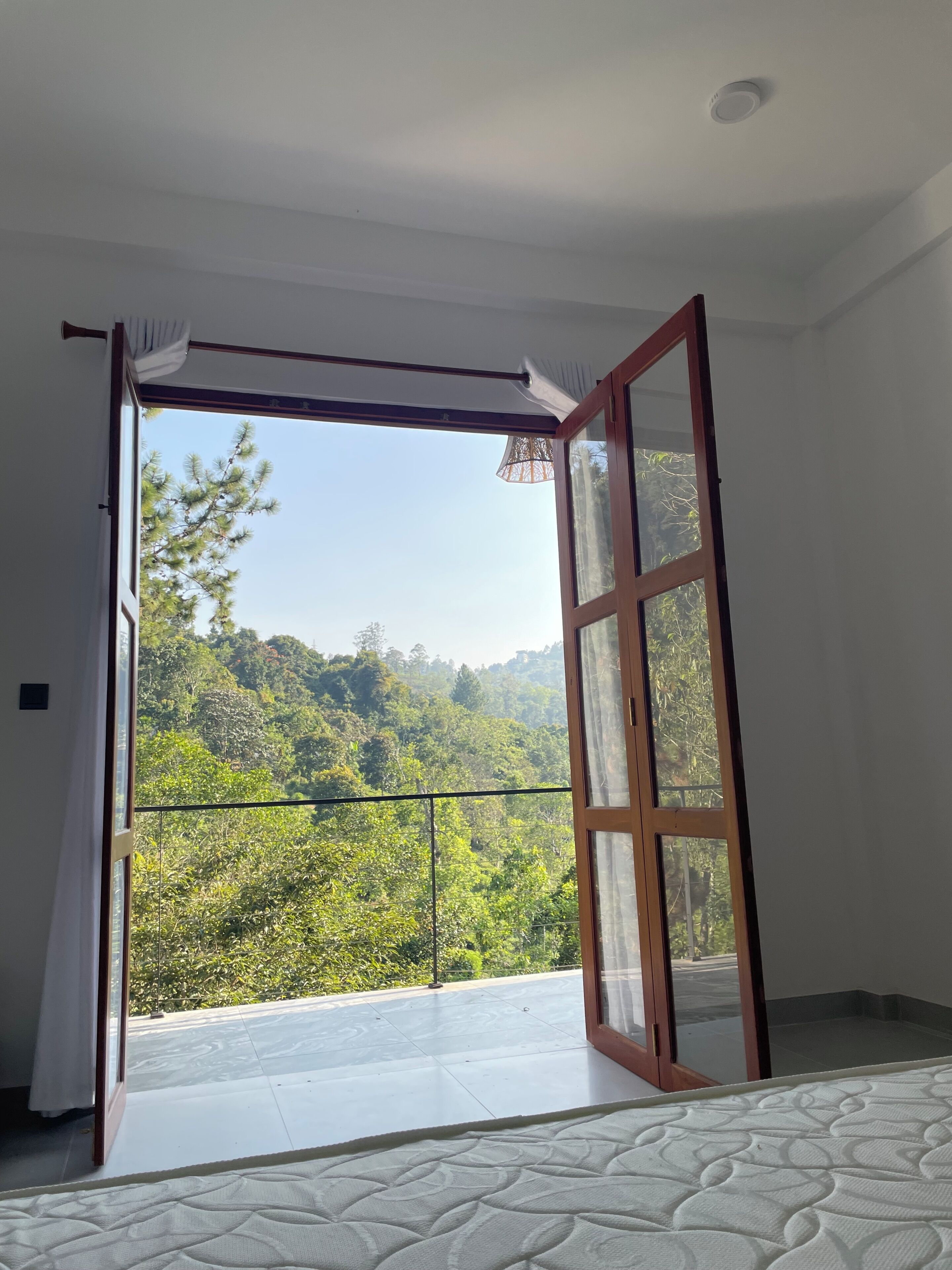 A room with a large sliding glass door leading to a balcony with a view of a forested hillside.