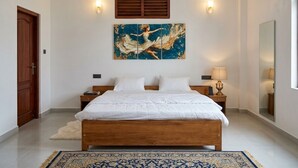 Un dormitorio con una cama de madera, un ventilador de techo, un cuadro abstracto grande, dos lámparas de noche y un espejo en la pared.