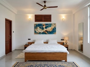 Ein Schlafzimmer mit einem hölzernen Bett, einem Deckenventilator, einem großen abstrakten Gemälde, zwei Nachttischlampen und einem Spiegel an der Wand.