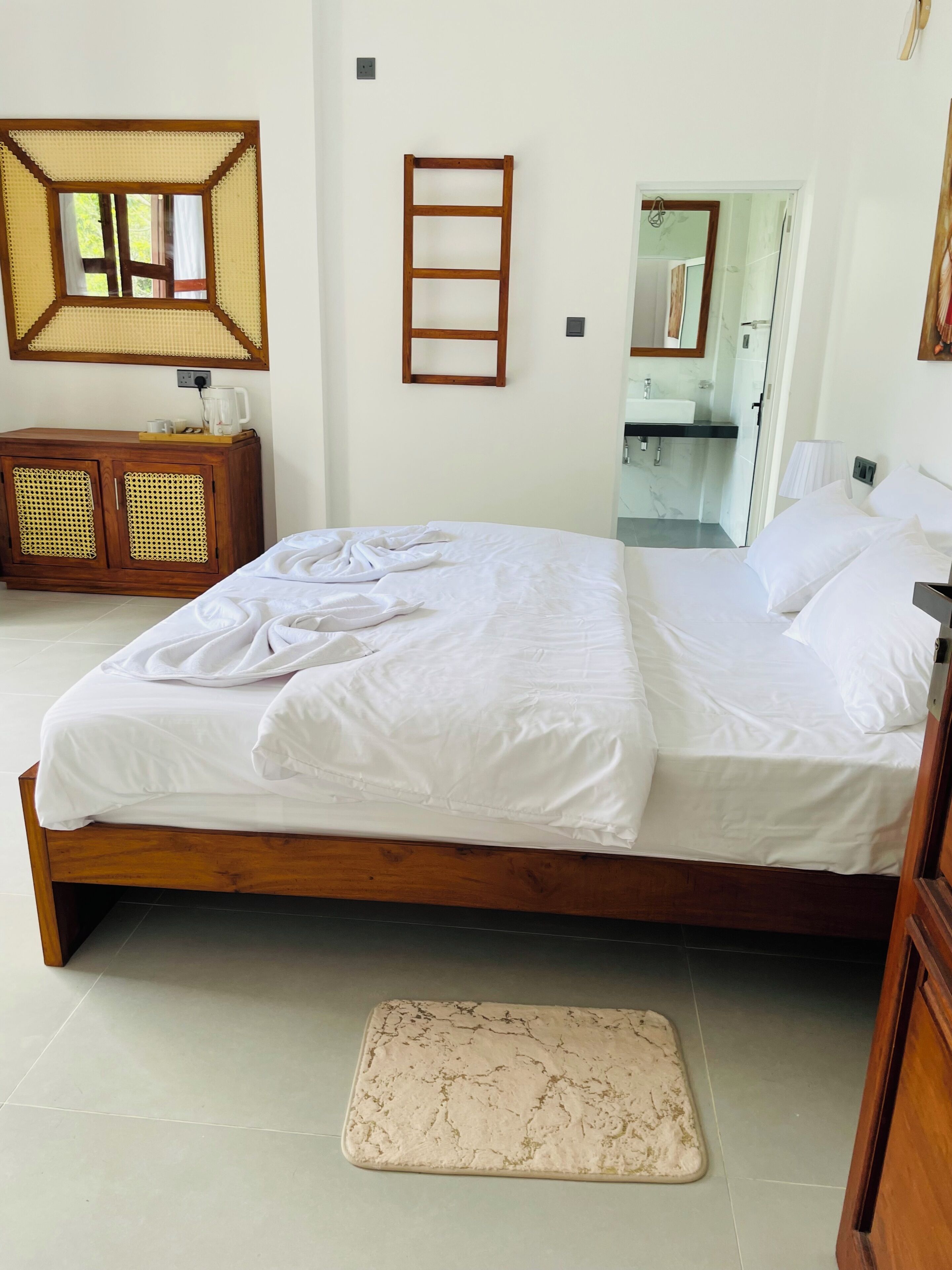 Une chambre à coucher avec un lit en bois, une table de chevet, un miroir et une salle de bain visible à travers une porte ouverte.
