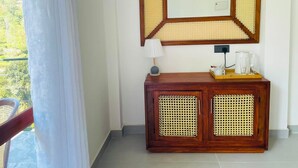 Una habitación con un armario de madera, un espejo de marco geométrico, una lámpara y una cafetera sobre una bandeja.
