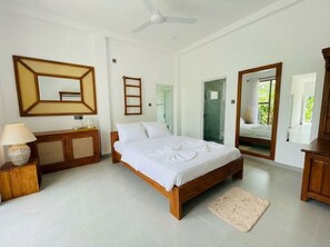 Une chambre à coucher avec un lit en bois, un ventilateur de plafond, un miroir, une armoire et une porte menant à la salle de bain.